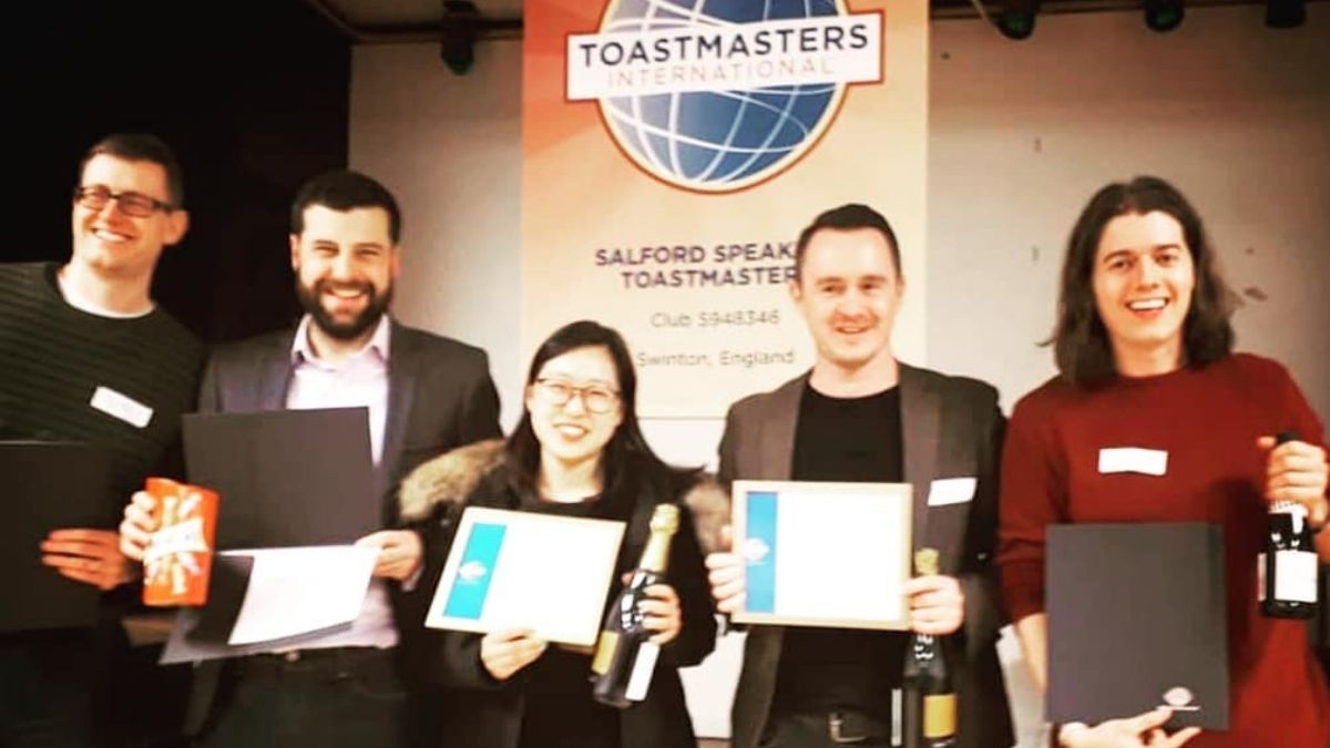 Group of professionals smiling and holding certificates after winning a Toastmasters competition, including Ed and Dan from Project Charisma