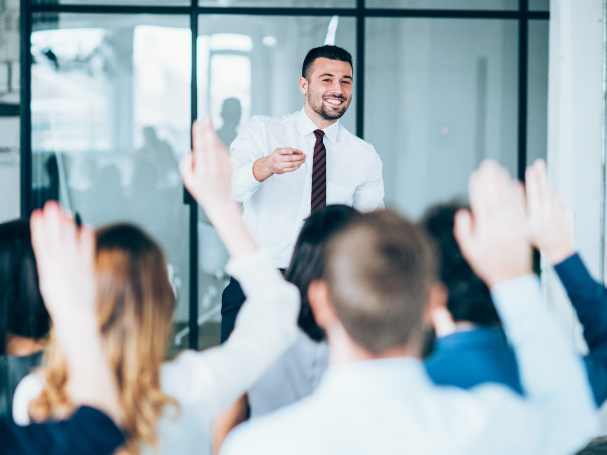 a man in a suit who is ready for public speaking training, addressing a room of people.