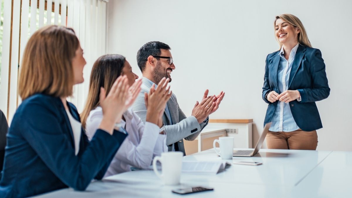 Woman smiling after finishing a presentation while her colleagues clap in appreciation