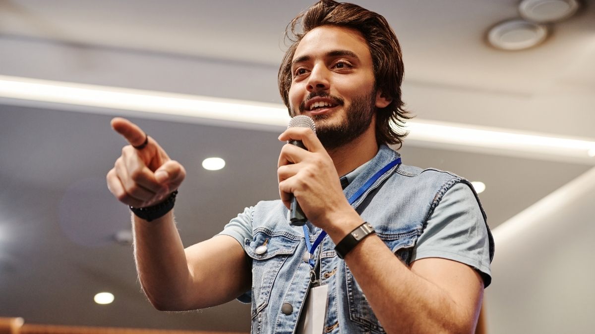 Man smiling while delivering a powerful speech opener with a microphone to his audience