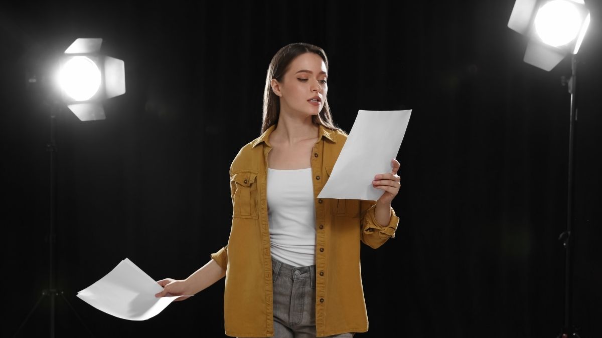 Woman on stage holds a script while preparing for a presentation