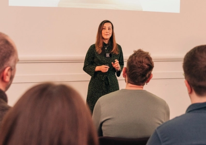 Professional woman delivering a keynote talk during Project Charisma’s 1-to-1 Charismatic Speaker Programme, with 1-to-1 coaching clients presenting to a small audience